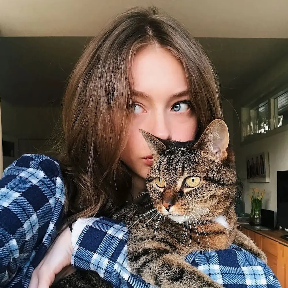 Home a cozy indoor selfie of a young woman with long, parted brown hair and striking blue eyes
